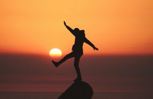 a person dancing on a rock with sunset on horizon