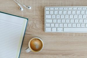 computer keyboard, notebook, ear buds, and coffee