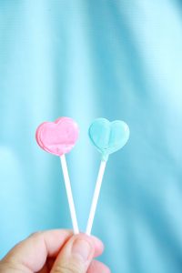 a hand holding pink and blue heart-shaped lollipop candy