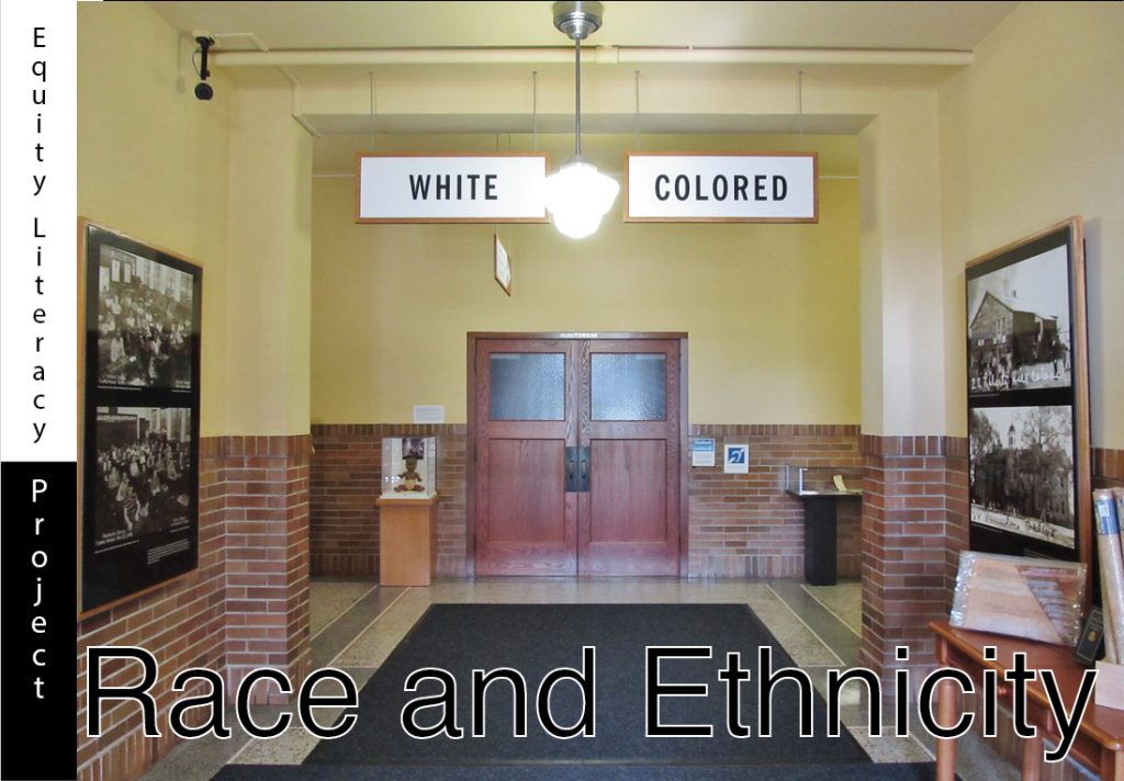 A photograph of a 1950’s style school hallway with a closed wooden double door in the distance. Two signs hang from the ceiling before the double doors that read White to the left and Colored to the right. The caption Race and Ethnicity in black text with white outline is placed beneath the photo. Photo is from the Brown vs Board of Education National Historic Site.