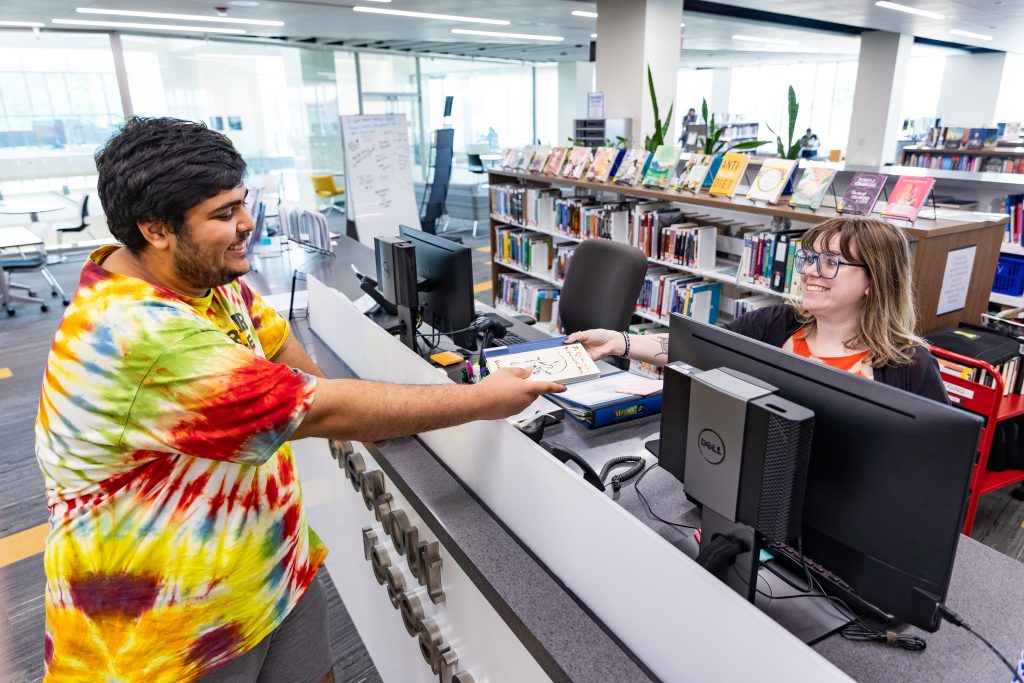library staff behind library desk handing a students in front of the desk a book